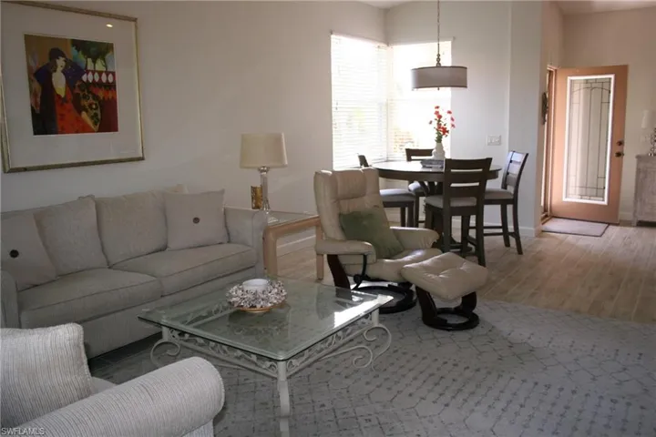 Open concept living and dining area featuring wood-finish flooring, white wall tones, and a front entry door with decorative glass inserts