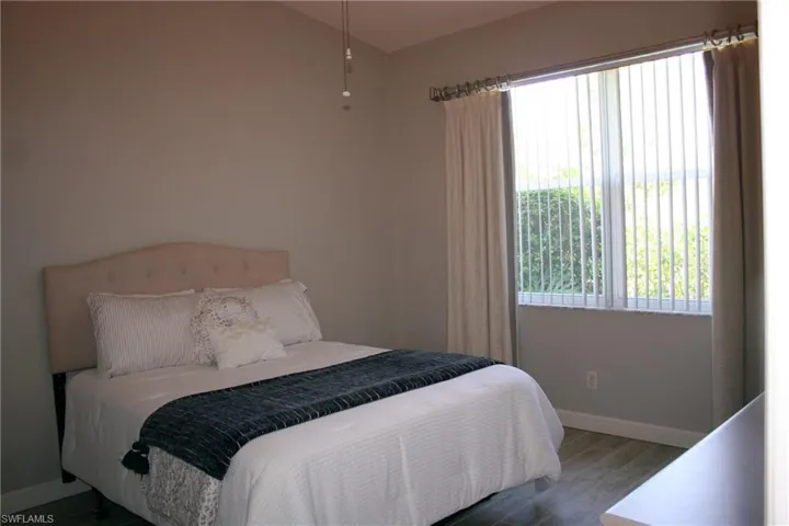 Room featuring vaulted ceilings, wood-finish flooring, a window with vertical blinds, and neutral wall paint