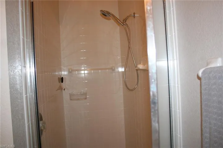 Shower enclosure featuring subway tile walls, a sliding glass door, and a handheld showerhead