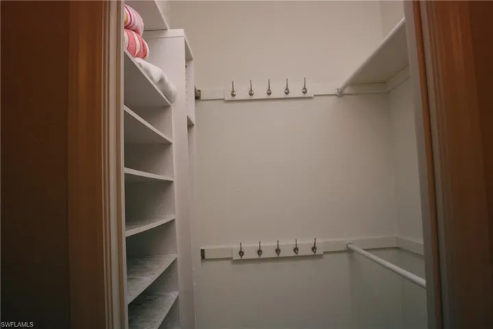 Walk-in closet featuring built-in shelving, a full-length clothes rod, and multiple wall-mounted hooks for storage