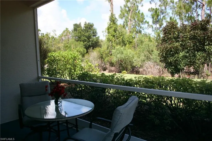 Screened patio with a stucco exterior, overlooking a landscaped shrub border and a natural tree line