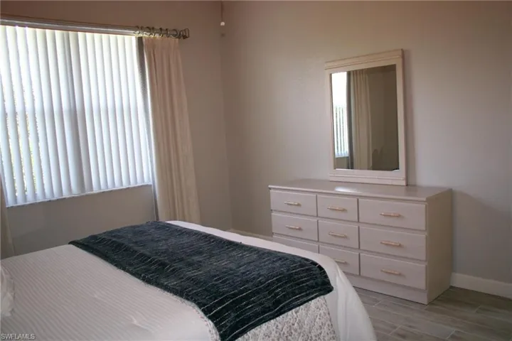 Room featuring light-colored walls, wood-finish flooring, a window with vertical blinds, and draperies