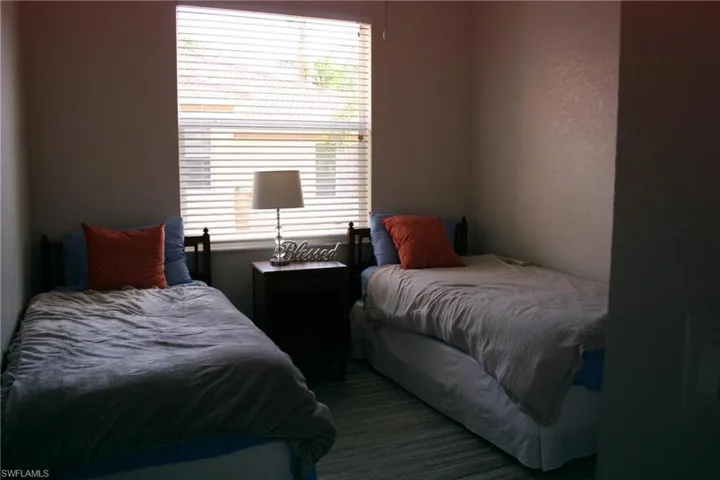 Bedroom with a window featuring horizontal blinds, wood-finish flooring, and light-toned walls