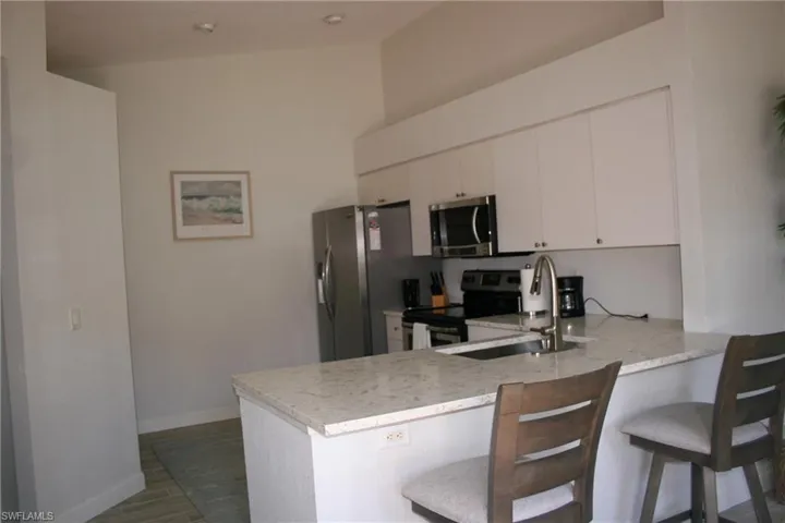 Modern kitchen featuring a breakfast bar with stone-finish countertops, stainless steel appliances, white cabinetry, and recessed lighting
