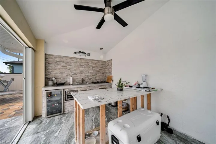 Kitchen featuring wine cooler, sink, ceiling fan, decorative backsplash, and vaulted ceiling