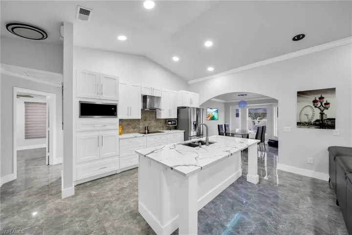 Kitchen with ventilation hood, white cabinets, a center island with sink, and ornamental molding