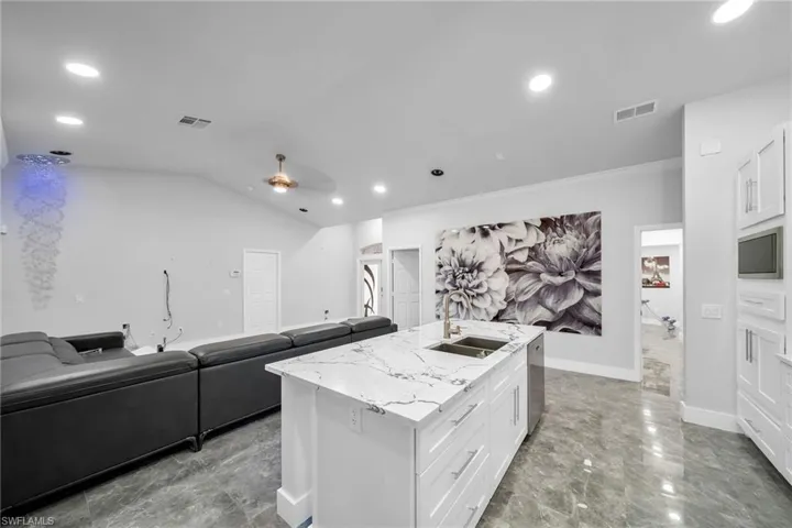 Kitchen with light stone countertops, a kitchen island with sink, sink, ceiling fan, and white cabinets