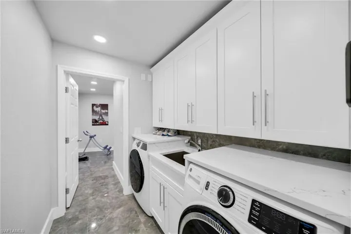 Clothes washing area with washing machine and clothes dryer, cabinets, and sink