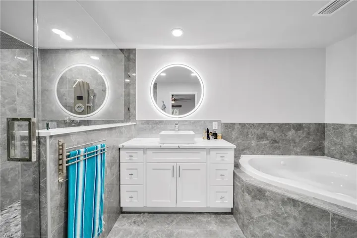 Bathroom featuring tile walls, shower with separate bathtub, and vanity