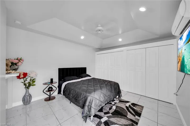 Bedroom with a raised ceiling, ceiling fan, and a wall unit AC