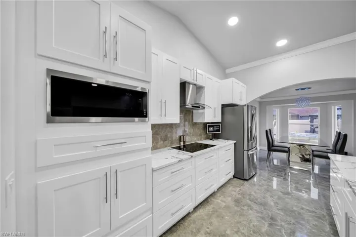 Kitchen featuring stainless steel appliances, light stone counters, lofted ceiling, white cabinets, and wall chimney range hood