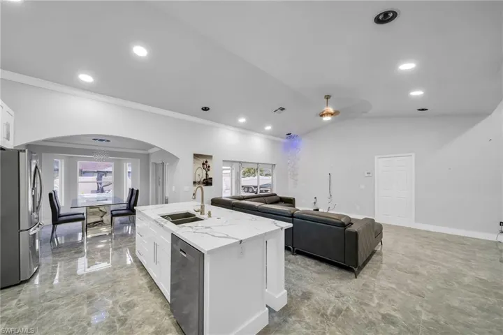 Kitchen with vaulted ceiling, a center island with sink, appliances with stainless steel finishes, white cabinetry, and ceiling fan