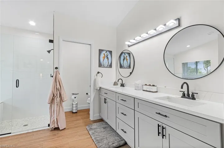 Full bath with double vanity, a shower stall, recessed lighting, and light wood-style floors