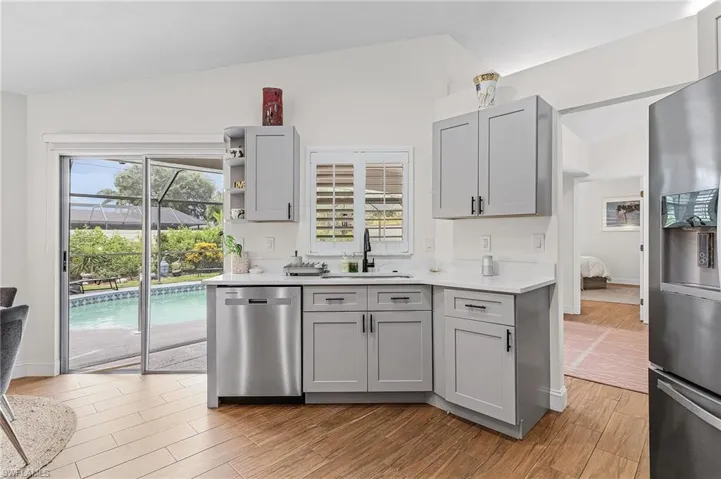 Kitchen featuring gray cabinets, stainless steel appliances, open shelves, light wood-style floors, and lofted ceiling