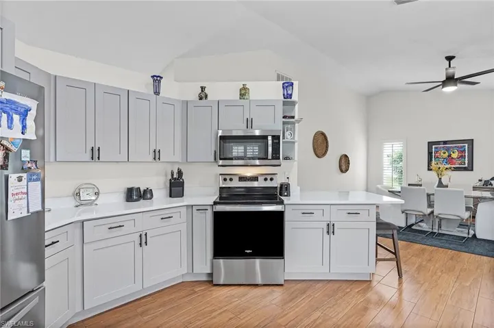 Kitchen featuring stainless steel appliances, a peninsula, vaulted ceiling, open shelves, and light wood-style flooring
