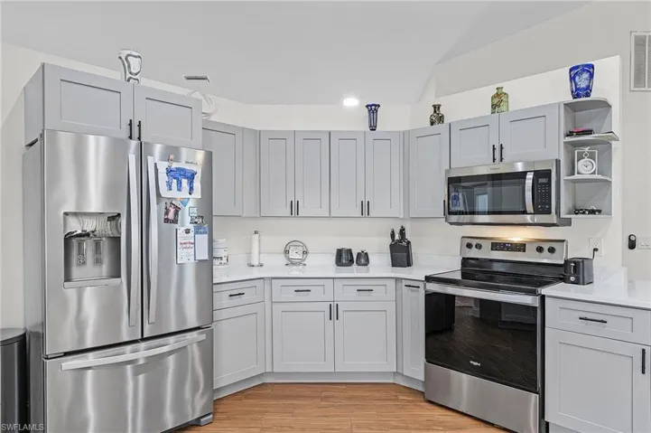 Kitchen featuring stainless steel appliances, open shelves, light wood-type flooring, and light stone countertops