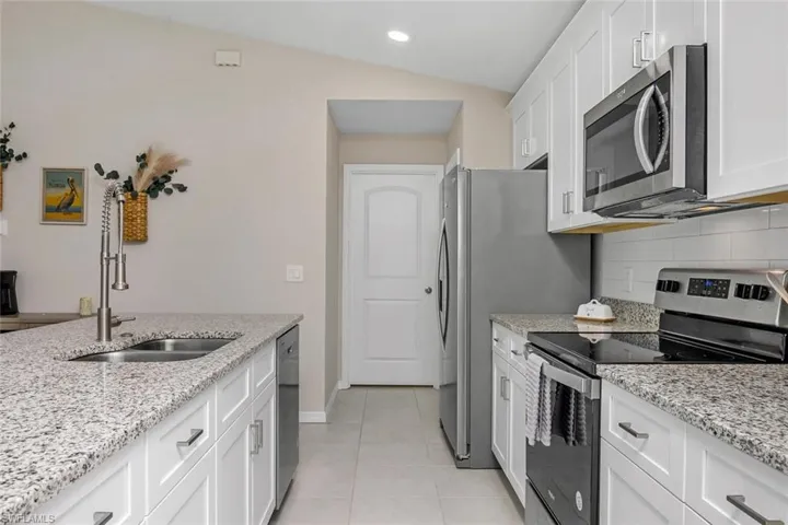 Kitchen with light tile patterned flooring, light stone countertops, appliances with stainless steel finishes, decorative backsplash, and vaulted ceiling