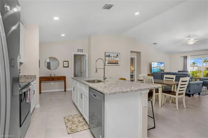 Kitchen with white cabinetry, light tile patterned flooring, stainless steel appliances, sink, and lofted ceiling