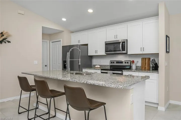 Kitchen featuring white cabinetry, decorative backsplash, stainless steel appliances, and an island with sink