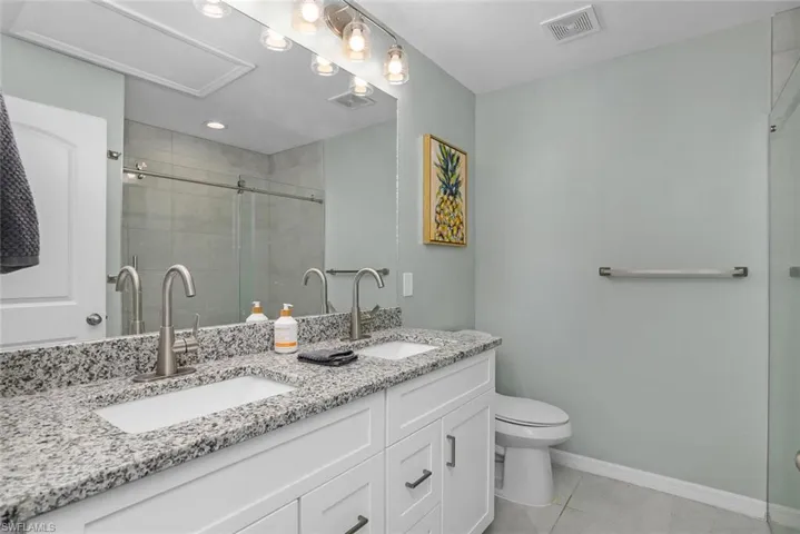 Primary Bathroom with toilet, a shower with door, double sink vanity, and tile patterned flooring