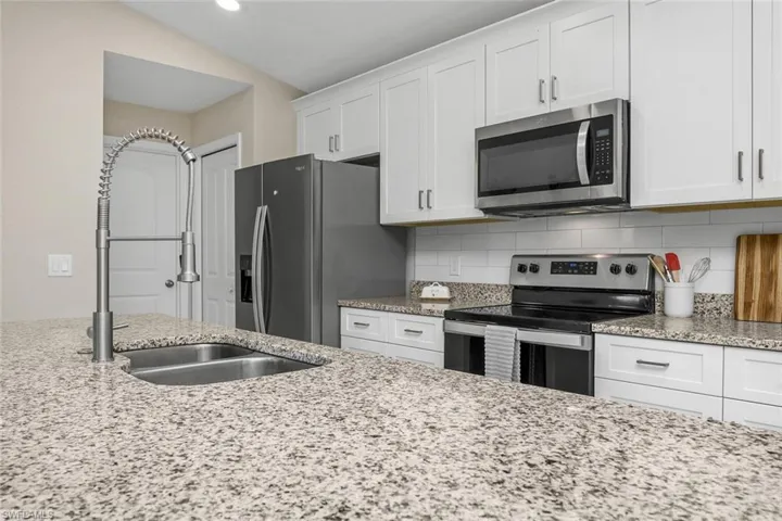Kitchen featuring white cabinetry, light stone countertops, stainless steel appliances, and backsplash