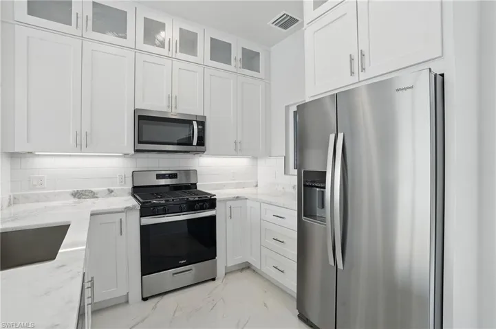 Kitchen with stainless steel appliances, light marble finish floors, white cabinets, light stone counters, and glass insert cabinets VIRTUALLY EDITED