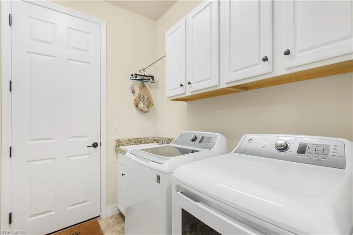 Clothes washing area with washer and clothes dryer, sink, and cabinets