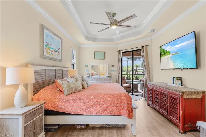 Bedroom with light hardwood / wood-style flooring, access to exterior, ceiling fan, a raised ceiling, and ornamental molding
