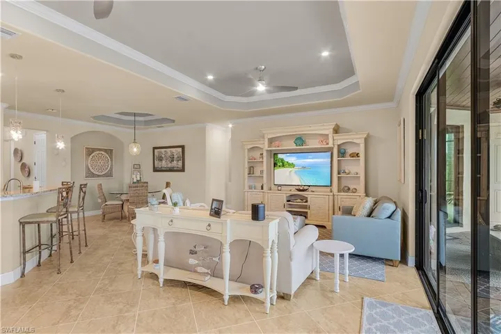 Tiled living room featuring a raised ceiling, ornamental molding, and ceiling fan