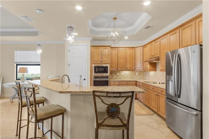 Kitchen featuring tasteful backsplash, stainless steel appliances, hanging light fixtures, a raised ceiling, and light tile patterned floors