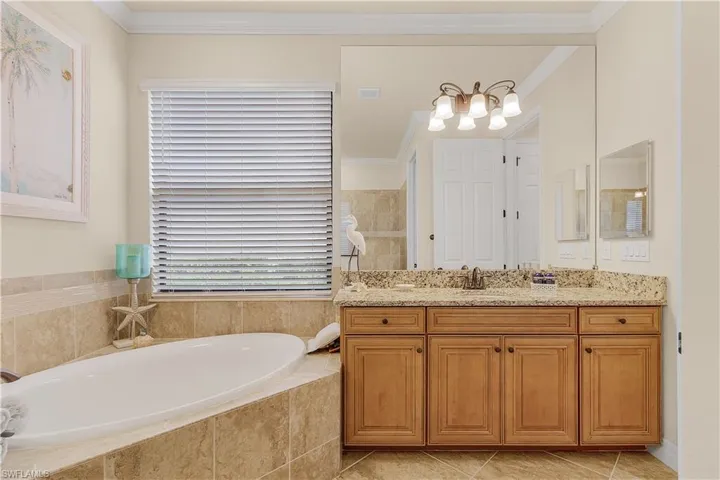 Bathroom with tiled tub, vanity, tile patterned floors, and crown molding