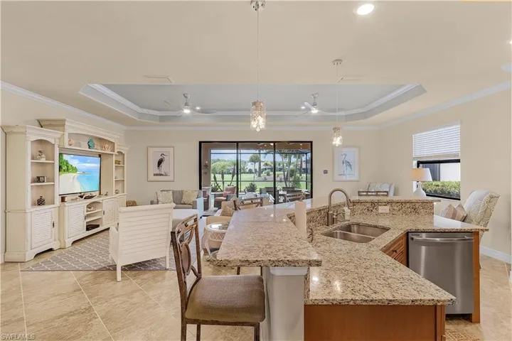 Kitchen featuring a kitchen island with sink, ceiling fan, and a tray ceiling