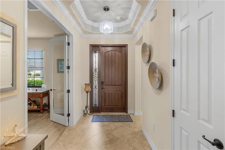 Entryway featuring an inviting chandelier, light tile patterned floors, a raised ceiling, and crown molding