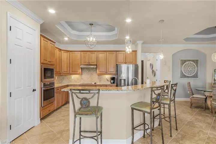 Kitchen featuring light tile patterned flooring, stainless steel appliances, hanging light fixtures, a raised ceiling, and ornamental molding