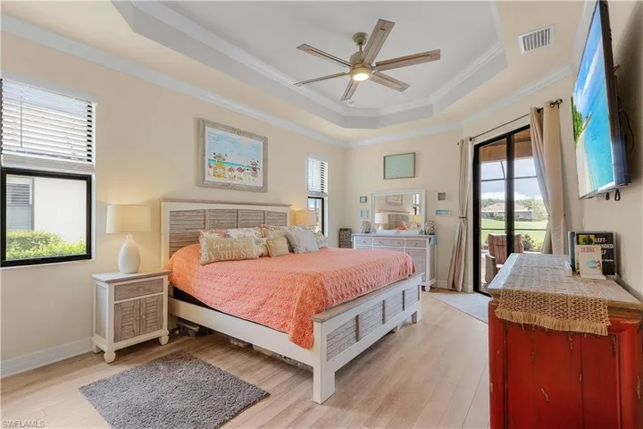 Bedroom with crown molding, light wood-type flooring, access to exterior, ceiling fan, and a raised ceiling