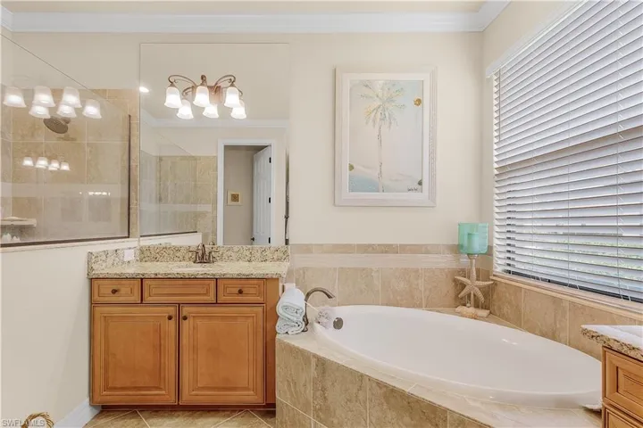 Bathroom featuring tiled tub, tile patterned floors, crown molding, and vanity