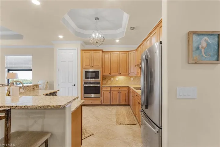 Kitchen with a tray ceiling, hanging light fixtures, stainless steel appliances, crown molding, and light tile patterned floors