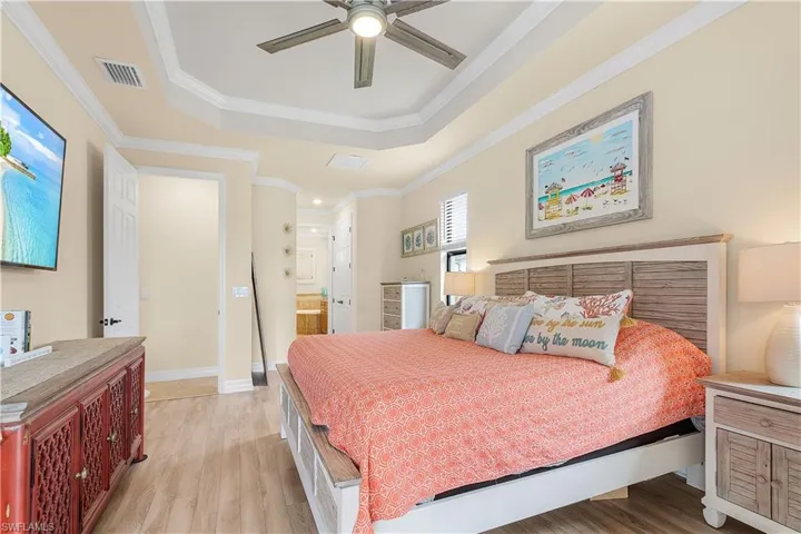 Bedroom with light wood-type flooring, a tray ceiling, connected bathroom, and ornamental molding