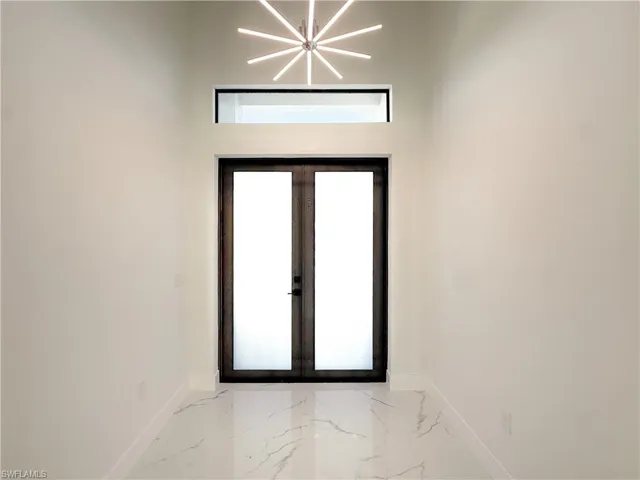 Foyer with french doors, light marble finish floors, and a chandelier