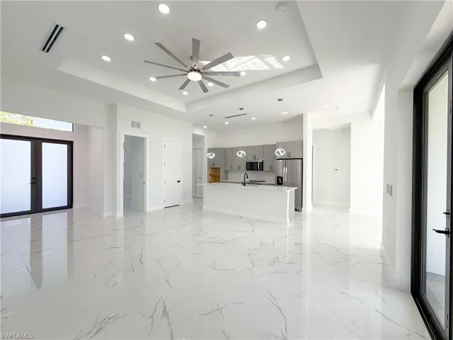 Unfurnished living room featuring a raised ceiling, recessed lighting, light marble finish flooring, ceiling fan, and french doors