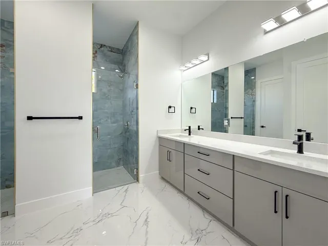 Full bathroom with a stall shower, double vanity, and light marble finish floors