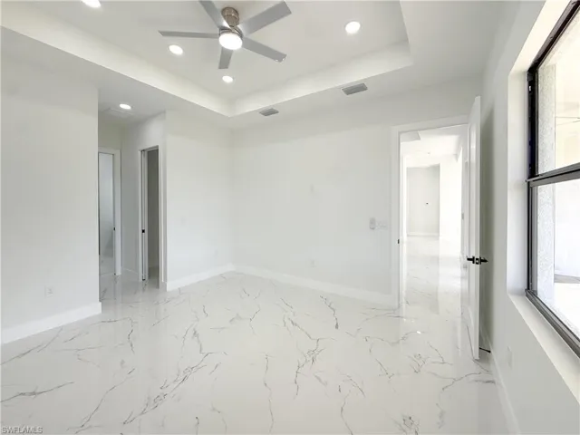Unfurnished room featuring recessed lighting, a tray ceiling, a ceiling fan, and light marble finish flooring