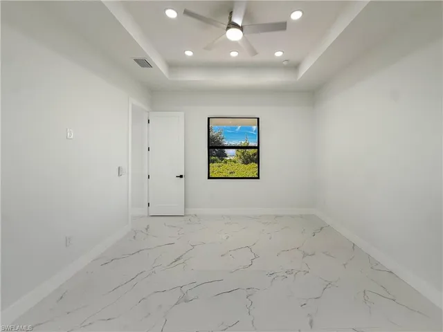 Unfurnished room with light marble finish floors, ceiling fan, recessed lighting, and a tray ceiling