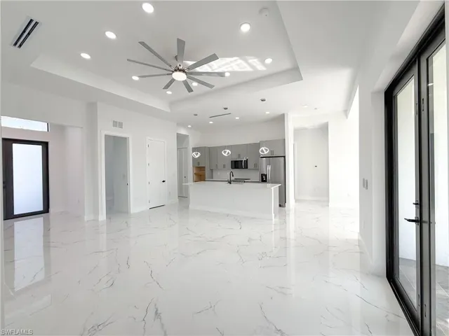 Unfurnished living room featuring recessed lighting, a raised ceiling, light marble finish floors, and a ceiling fan
