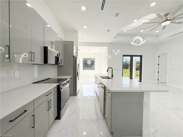 Kitchen featuring gray cabinets, hanging light fixtures, stainless steel appliances, light stone counters, and an island with sink