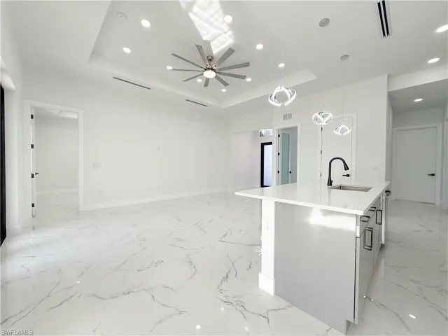 Kitchen with a kitchen island with sink, pendant lighting, recessed lighting, light stone countertops, and light marble finish floors