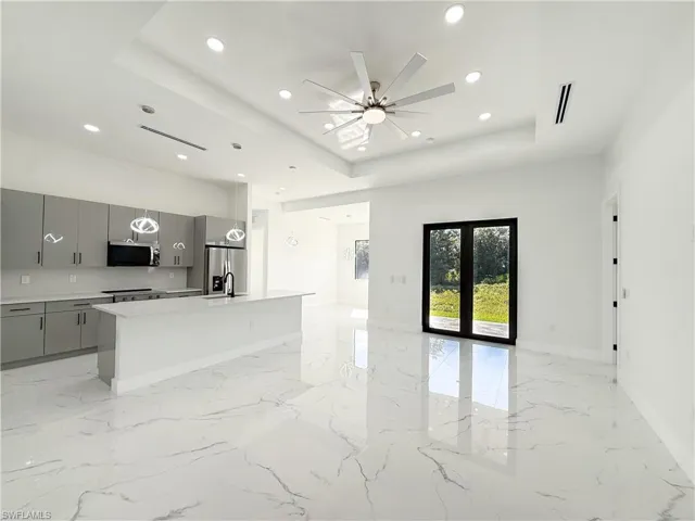 Kitchen with a center island with sink, decorative light fixtures, open floor plan, a tray ceiling, and stainless steel appliances