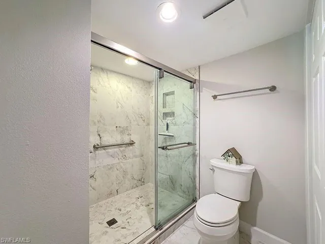 Bathroom featuring a shower with door and toilet