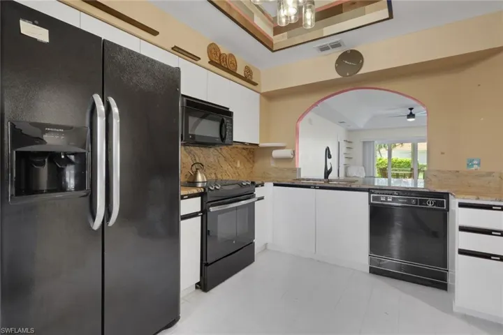 Kitchen featuring white flat-panel cabinetry, stone-surface countertops, black appliances, and a decorative arched pass-through window