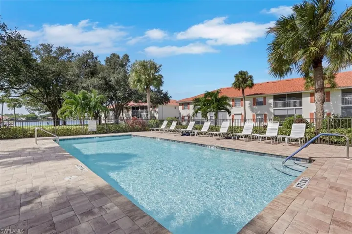In-ground swimming pool featuring a paver stone deck, metal perimeter fencing, and mature palm landscaping